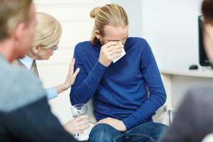 young man sitting in circle of psychological support group crying while sharing his trouble with mentor and other participants